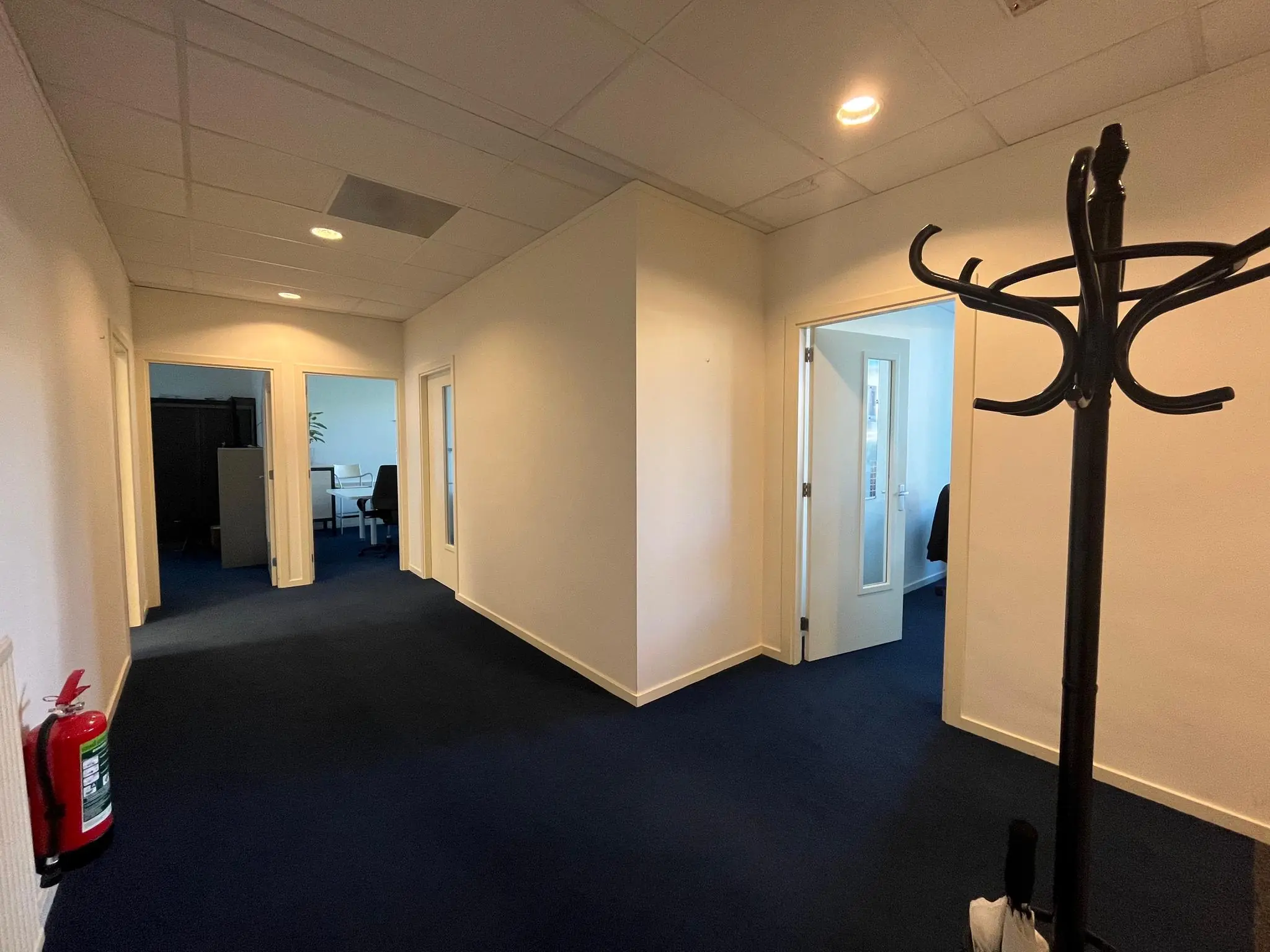 Verlichte kantoorhal aan de Jan van Eycklaan met open deuren naar meerdere kantoorruimtes en een kapstok op de voorgrond.